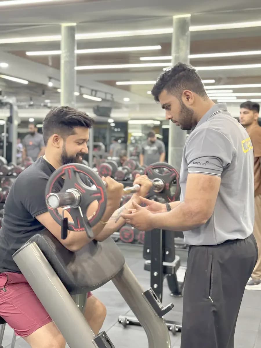 A trainer correcting a member's form on a cable machine